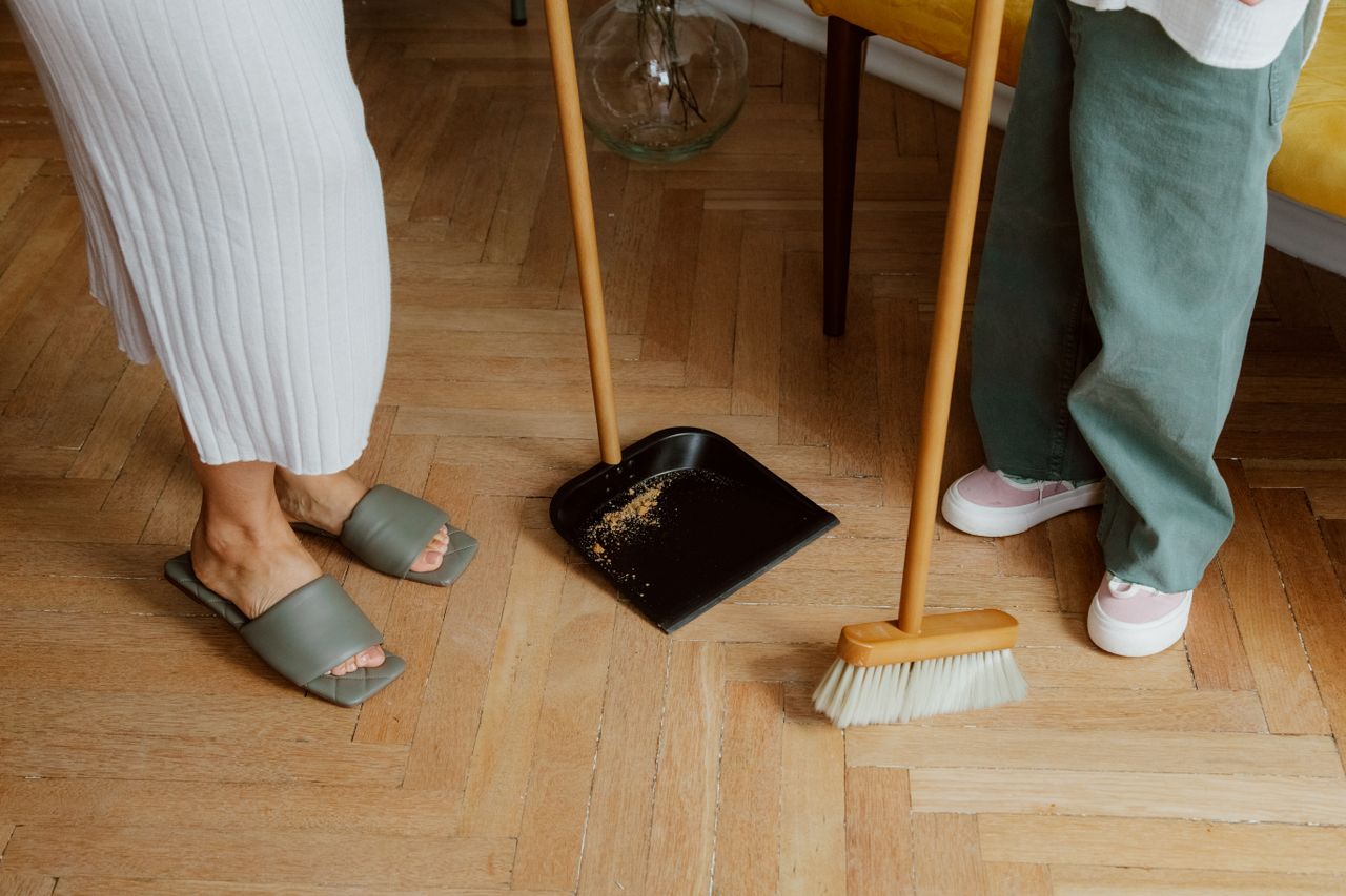 services-03 A mother and child cleaning the floor with a broom and dustpan indoors.